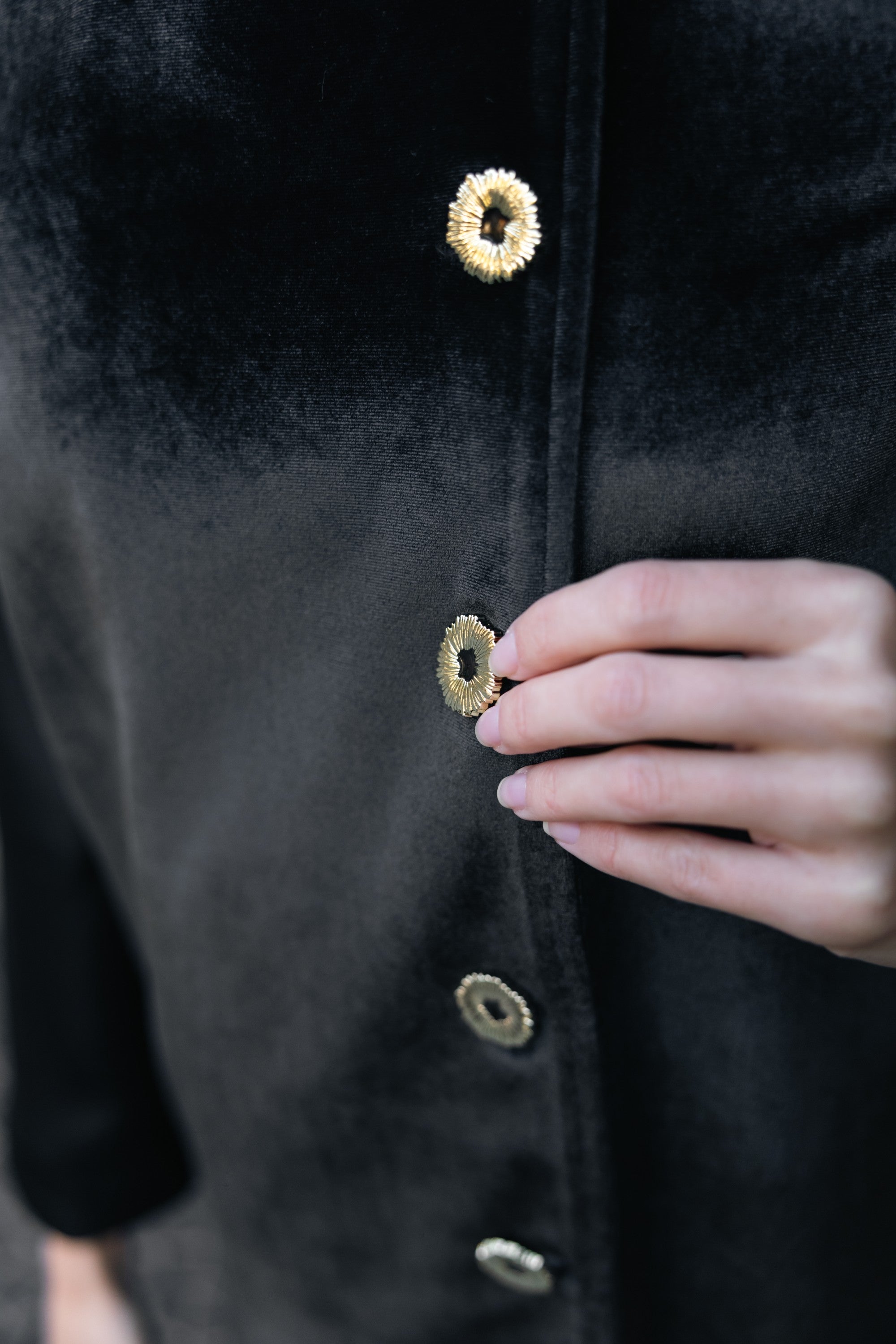 Close-up of a black coat with gold buttons being buttoned by a hand. Office outfit. Work outfit. business outfit. Women suit. 