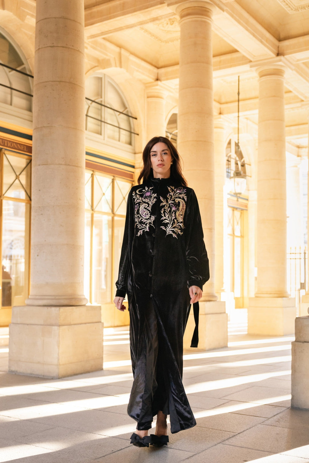 Woman in a black outfit with floral embroidery standing in a grand architectural setting in Paris.