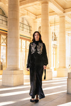 Woman in a black outfit with floral embroidery standing in a grand architectural setting in Paris.