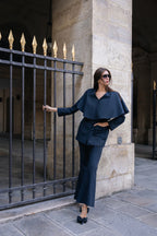 Woman in a pinstripe suit outfit standing next to a stone building with a metal gate in Paris.