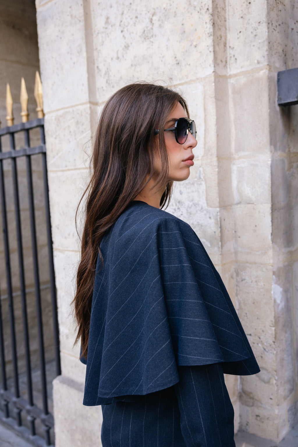 Woman wearing a dark blue pinstripe outfit standing against a stone wall.