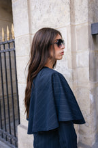 Woman wearing a dark blue pinstripe outfit standing against a stone wall.