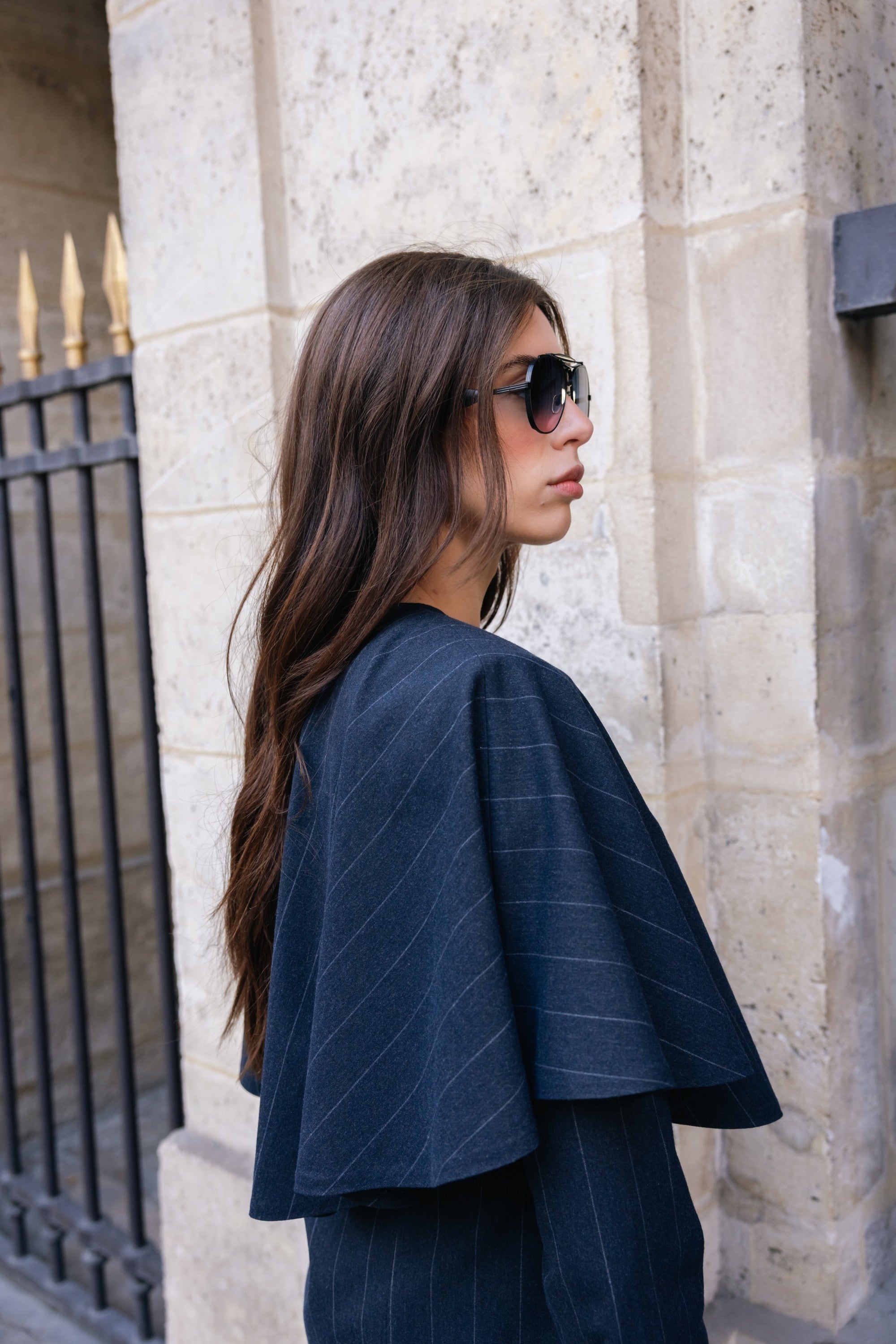Woman wearing a dark blue pinstripe outfit standing against a stone wall.