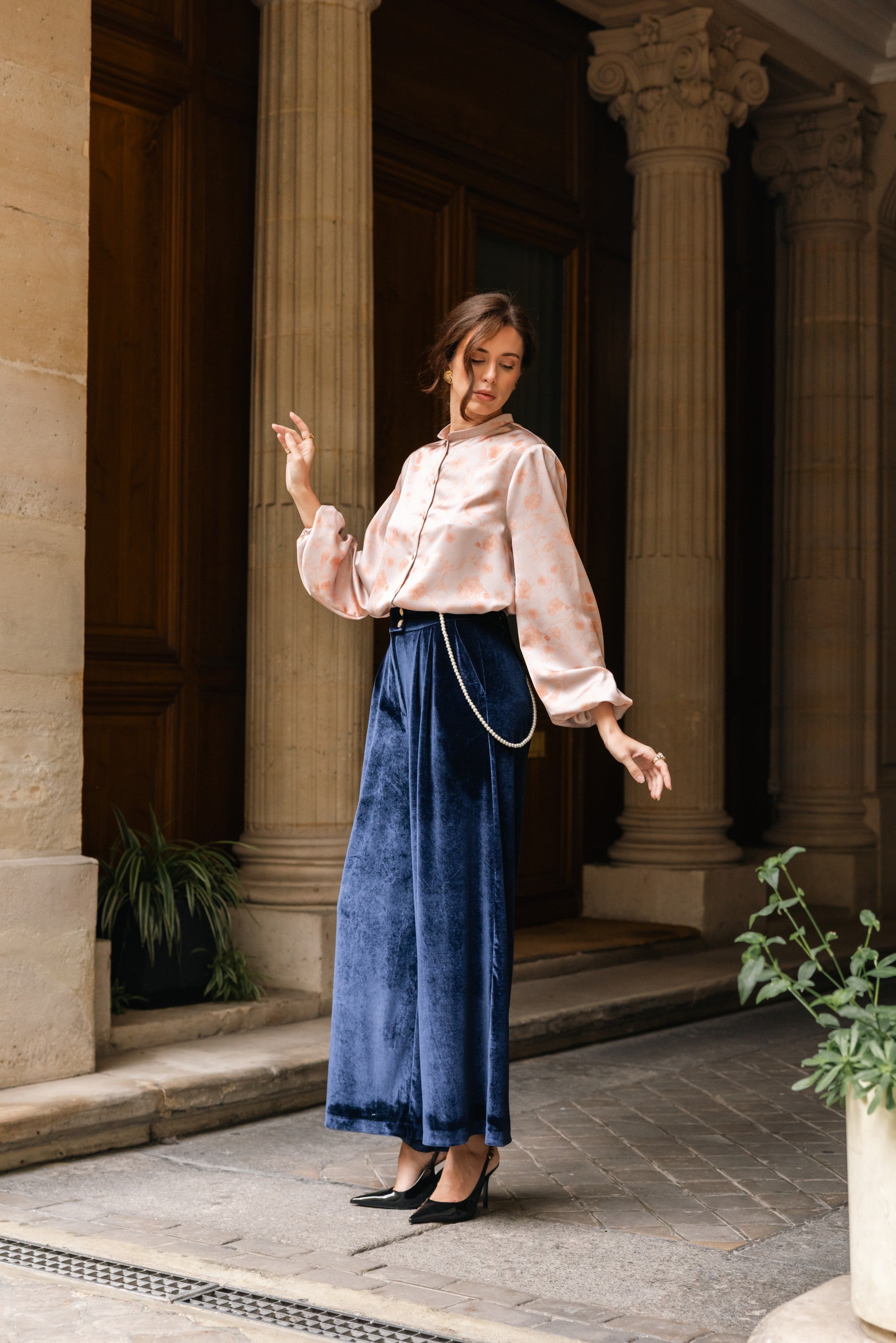 Woman in a pink blouse and blue pants standing in front of classical architecture.