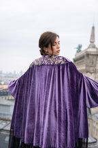 Woman wearing a purple velvet cape with floral embroidery in an urban setting