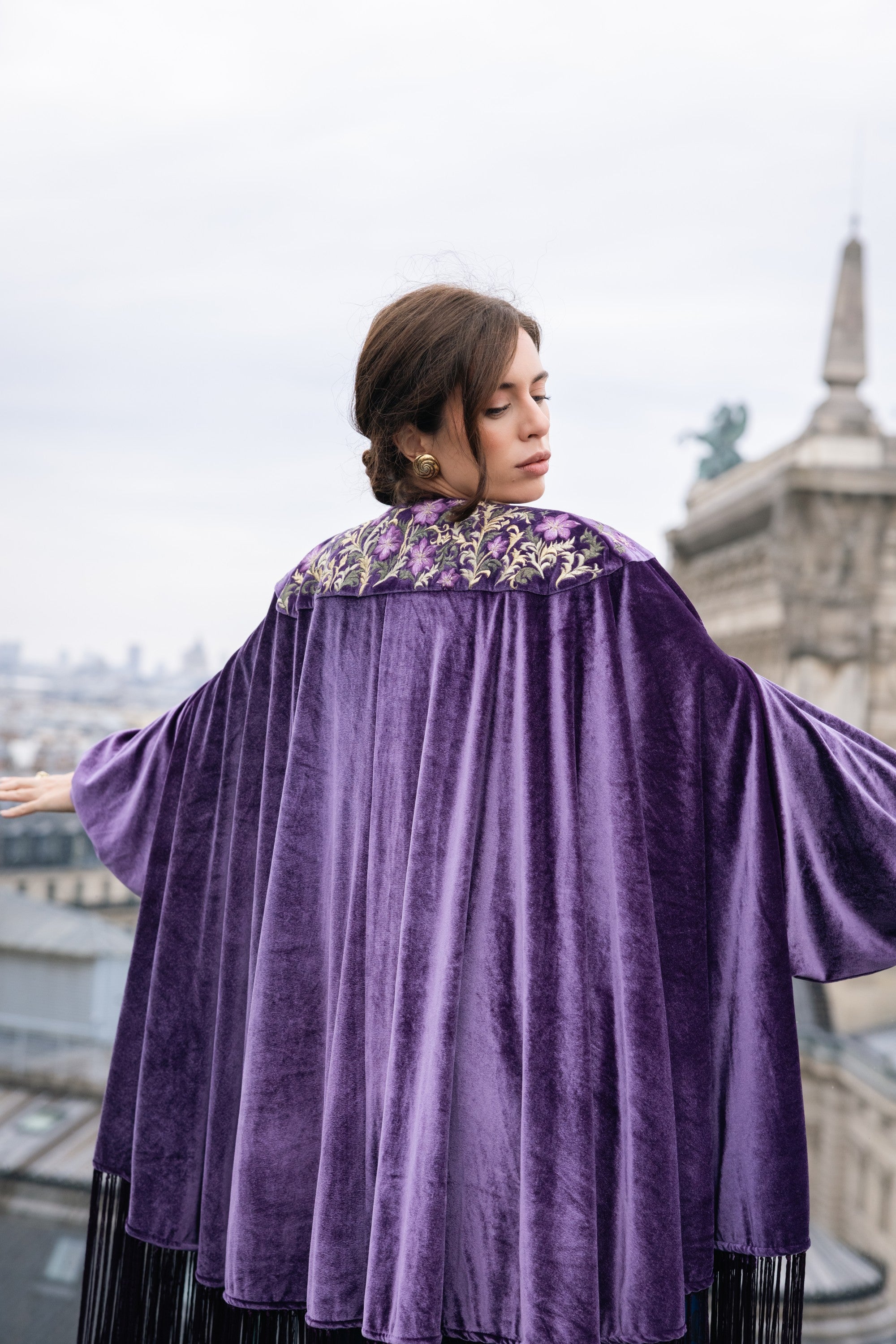 Woman wearing a purple velvet cape with floral embroidery in an urban setting