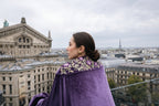 Woman in a purple velvet coat with floral embroidery overlooking the Parisian cityscape with notable architecture. 