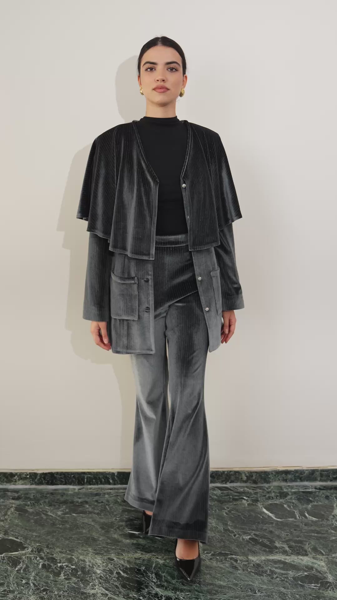 Woman in dark silver velvet suit outfit sitting on a textured chair in a room with decorative elements. Eid outfit, christmas outfit. party outfit